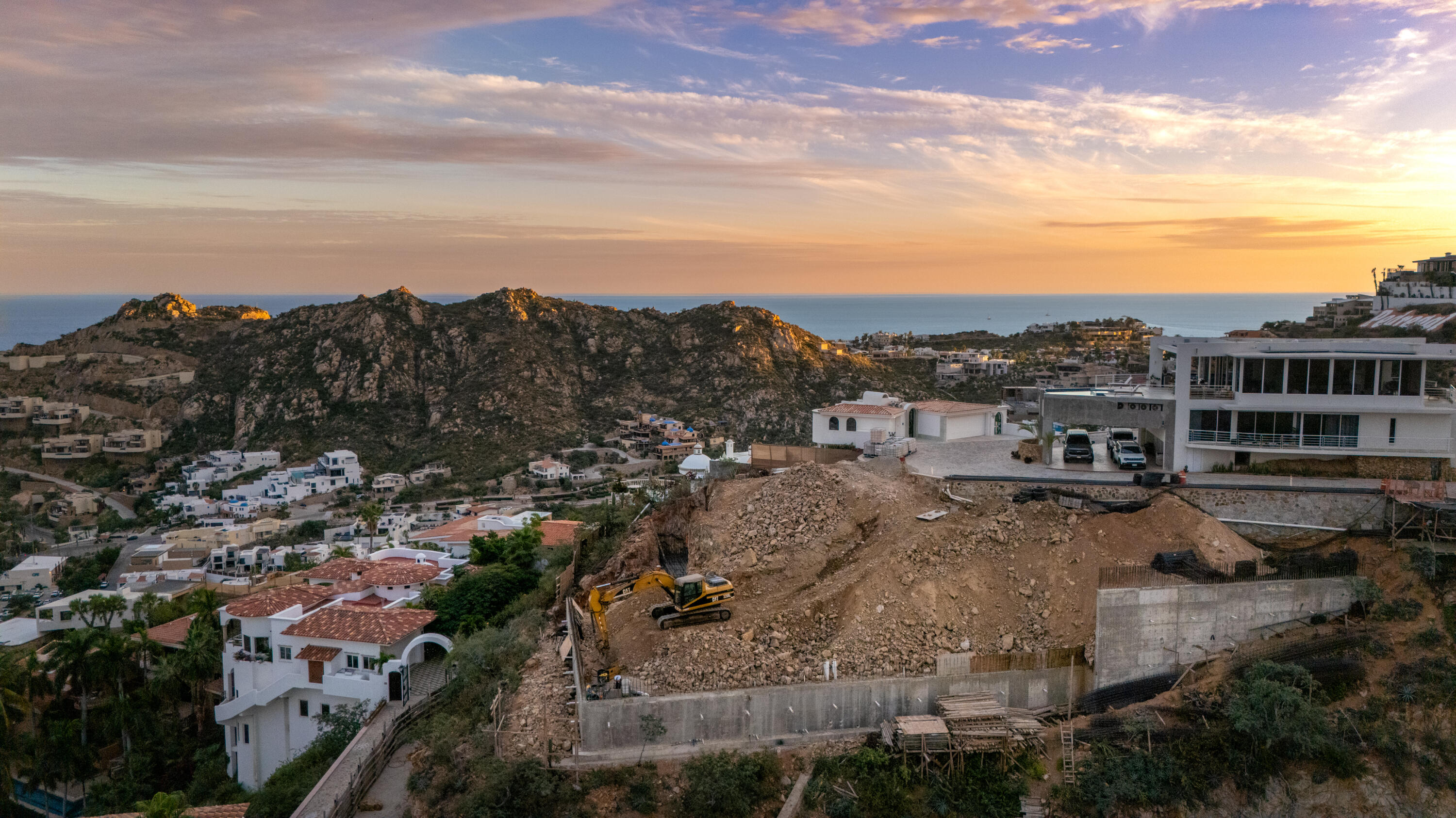Villa del León foundation walls in Pedregal, Cabo — excavator and ocean on the horizon